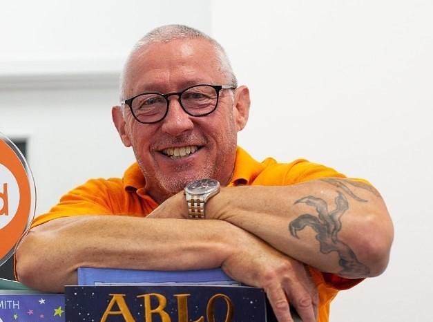 Gerry Durkin leaning over a book case and smiling